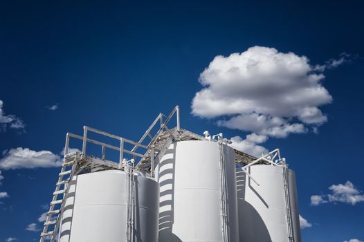 Image of industrial storage tanks against blue sky with clouds