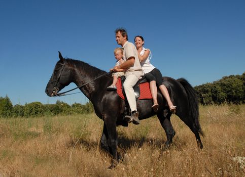 father, mother and son riding on a black horse