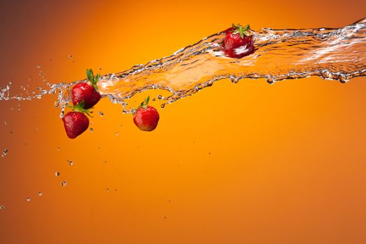 water splash with ripe red strawberry over orange background