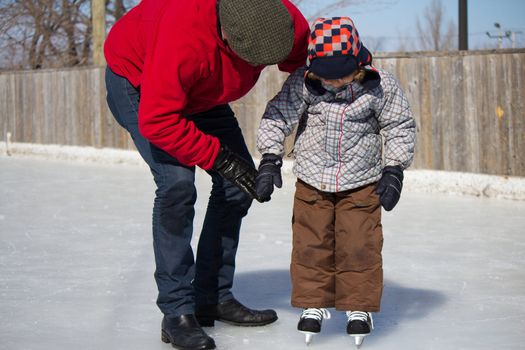 Father teaching son how to ice skate at an outdoor skating rink in winter.