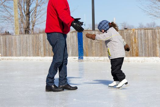 Father teaching daughter how to ice skate at an outdoor skating rink in winter.