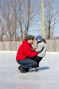 Father teaching daughter how to ice skate at an outdoor skating rink in winter.