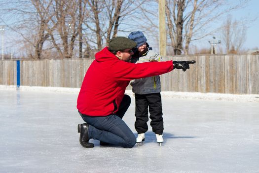 Father teaching daughter how to ice skate at an outdoor skating rink in winter.