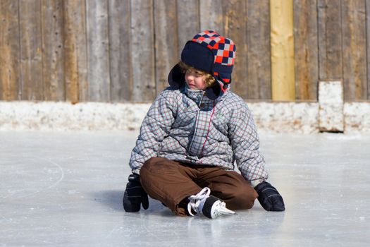 Boy learning to ice skate at an outdoor skating rink in winter.