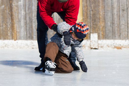 Father teaching son how to ice skate at an outdoor skating rink in winter.