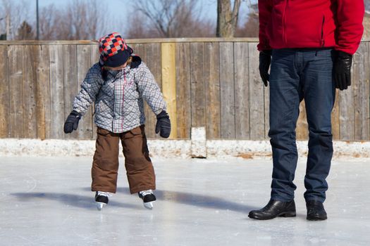 Father teaching son how to ice skate at an outdoor skating rink in winter.