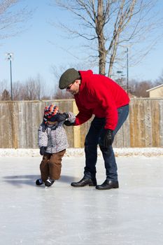 Father teaching son how to ice skate at an outdoor skating rink in winter.