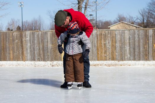 Father teaching son how to ice skate at an outdoor skating rink in winter.