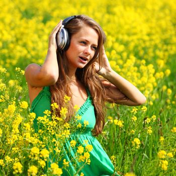  Young woman with headphones listening to music on oilseed flowering field