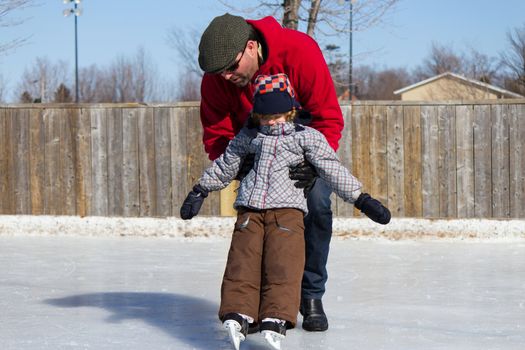 Father teaching son how to ice skate at an outdoor skating rink in winter.