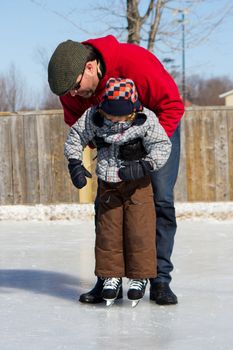 Father teaching son how to ice skate at an outdoor skating rink in winter.