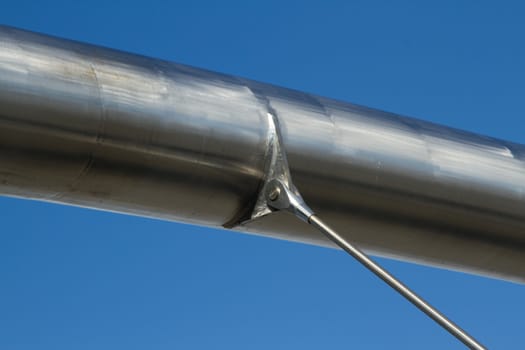 A large stainless steel tubular metal strut with a bracket and attachment to a metal rod against a bright blue sky.