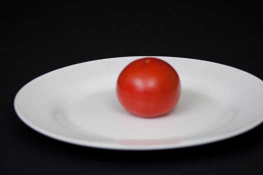 A red tomatoe on a white plate with a black background.