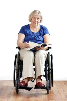 Happay disabled or handicapped senior woman in wheelchair, reading a book, looking at camera.