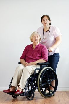 Senior woman in wheelchair at nursing home with middle-age nurse or aid.