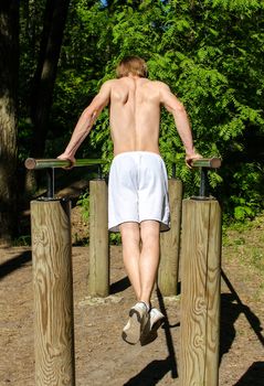 Man pull-ups on a bar in a forest. From the back.