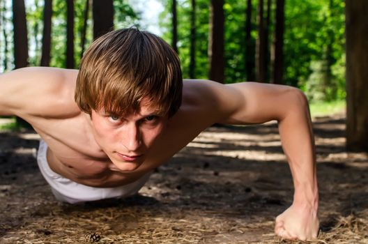 Attractive man doing a push up in forest