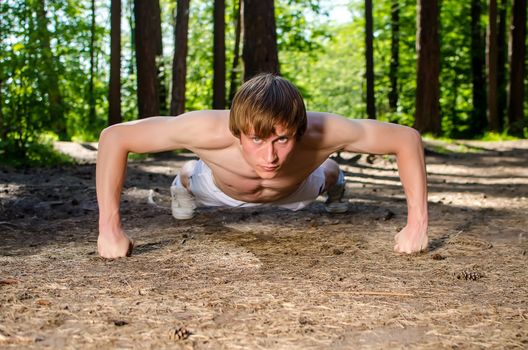 Attractive man doing a push up in forest