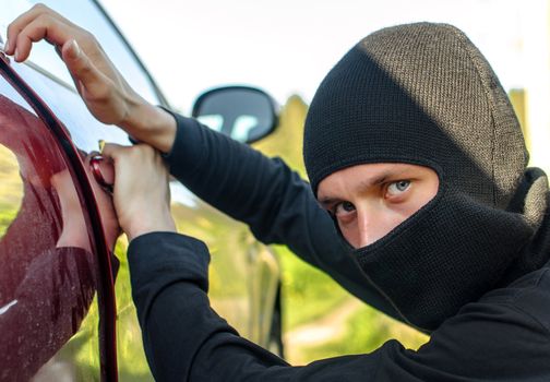 Thief in the mask breaks the door in the car