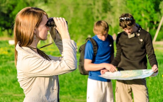 Three friends traveling. Girl looking through binoculars