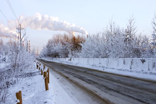 Snow-covered road to an environment of trees with smoking pipes on a background