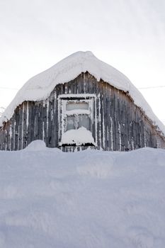 roof and window of a wooden small house covered with snow in the cold winter afternoon