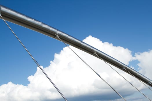 A large stainless steel tubular metal support structure with brackets and attachments to metal rods against a bright blue sky with cloud..