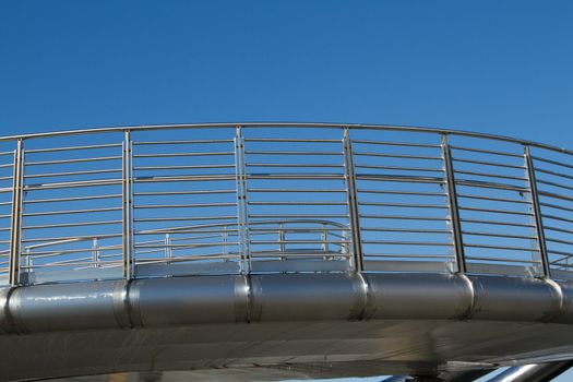 A raised section of a walkway made of stainless steel with safety hand rails against a clear blue sky.