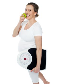 Young pregnant woman enjoy fresh green apple and holding weighing scale in other hand hand