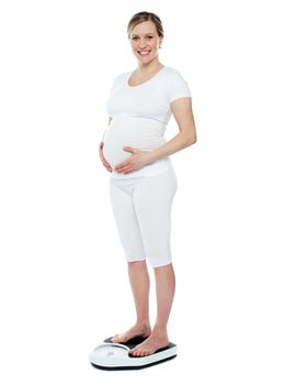 Pregnant woman measuring her weight through weighing scale. Hands on stomach