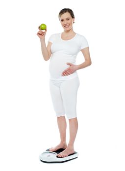 Pregnant woman standing on weighing machine showing fresh juicy green apple
