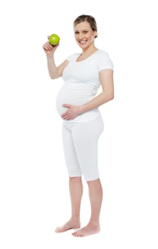 Pregnant woman showing fresh green apple while holding her belly. Isolated over white background