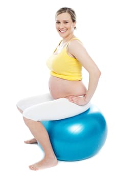 Pregnant woman exercises with big blue gymnastic ball. Smiling and looking at camera