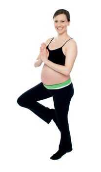 Portrait of beautiful pregnant woman doing yoga. Standing on one leg isolated against white background