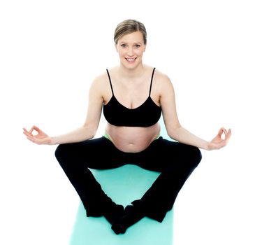 Beautiful pregnant woman in lotus pose, exercising on blue carpet
