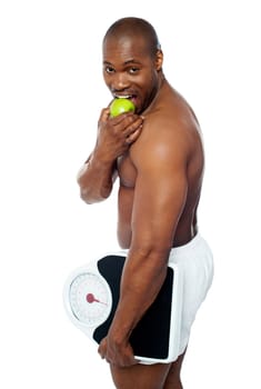 Young man enjoying fresh green apple and holding weighing scale in one hand