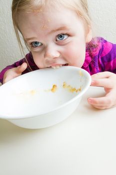 Young girl trying to eat her bowl after not being given enough food to eat.