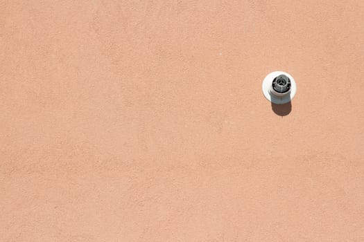 The vent from an extractor fan on a peach coloured textured wall.