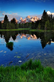 A reflection of Grand Teton Mountains with green grass