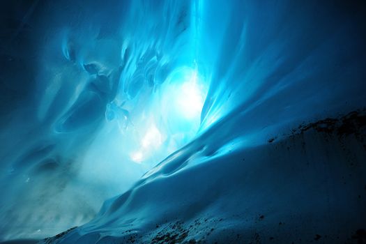 Light in a blue ice cave with curves of ice on the wall, from Root Glacier, Alaska