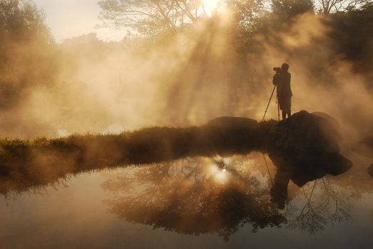 a photographer shadow in mist from hot spring in Thailand during sunrise