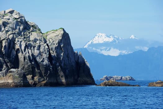 A rock standing on a sea with snow mountain, from Alaska