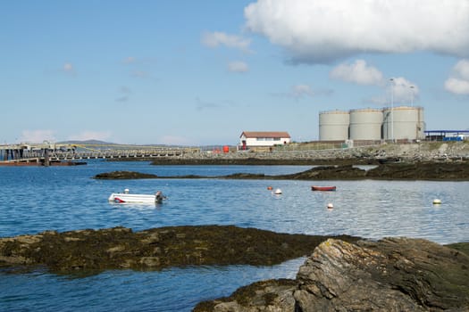 Storage tanks and buildings make up an industrial marine complex with the sea and boats in the foreground.