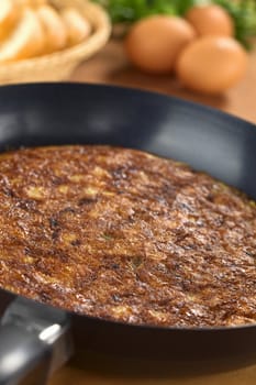 Preparing Spanish tortilla (omelette with potatoes) in frying pan with eggs and bread slices in the back (Selective Focus, Focus one third into the pan)