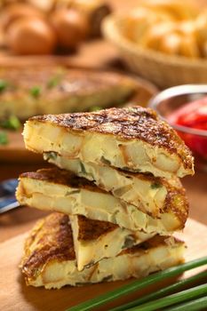 Fresh homemade Spanish tortilla (omelette with potatoes and onions) slices piled on wooden cutting board (Selective Focus, Focus on the front upper edge of the upper tortilla slice)