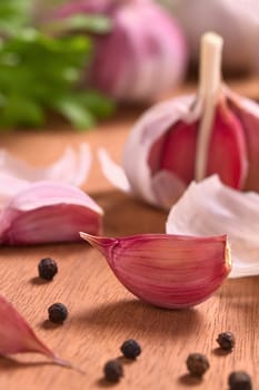 Garlic cloves with black pepper corns on wooden surface (Selective Focus, Focus on the front of the garlic clove on the right)