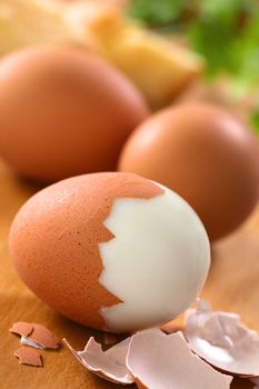 Fresh hard boiled eggs with shell beside on wooden board (Selective Focus, Focus on the front of the shell on the first egg)