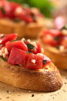 Fresh homemade crispy Italian antipasto called Bruschetta topped with tomato, garlic and basil on wooden board (Selective Focus, Focus on the front upper edge of the bruschetta and the lower part of the tomato pieces in the front) 