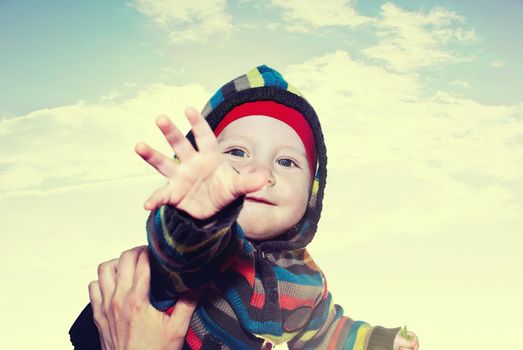 Happy boy on his hands at the mother to the sky with clouds.