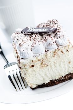 Tiramisu cake on white saucer with coffee cup background